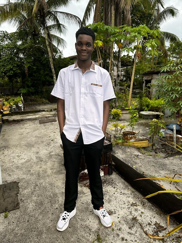 A picture of myself on vacation in Guyana, posing in front of a tropical backyard